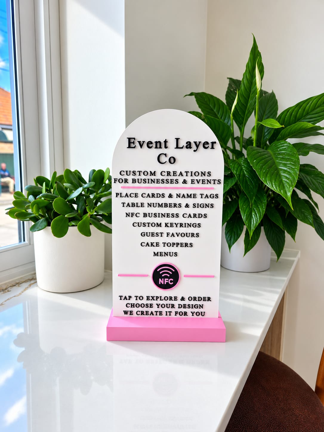 White arched Event Layer Co sign with raised black lettering and a pink NFC tap point